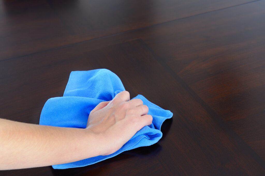 A woman holding a blue cloth cleaning a wooden table.